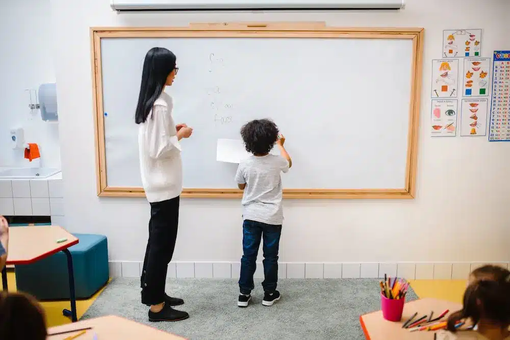 A teacher guiding a student to write on the whiteboard.
